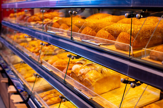 Supermarket bakery section with warm lighting, featuring fresh bread, buns, and homemade pastries on display shelves. Cozy bakery atmosphere.