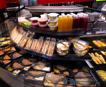 Supermarket display with packaged ready meals, sandwiches, salads, and juices. Convenient takeaway food section in grocery store.