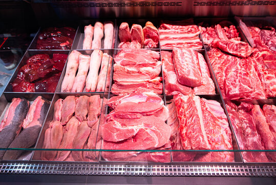 Supermarket meat counter with assorted pork cuts including pork neck, ham, liver, tongues, and pork feet displayed in refrigerated section.