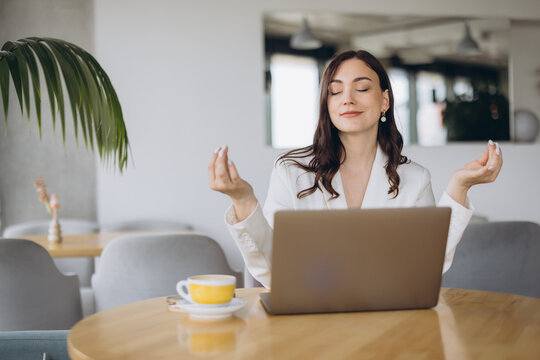 Businesswoman meditating at desk with laptop and coffee cup, finding a mindful moment during busy work