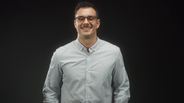 Hispanic man with moustache and glasses smiles and forms a triangle with his fingers while wearing a striped shirt in studio; approachability warmth friendly.
