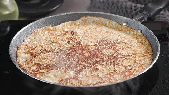 cook remove freshly baked crepe from hot frying pan with spatula in kitchen. process of making delicious pancakes at home for healthy breakfast, food close up