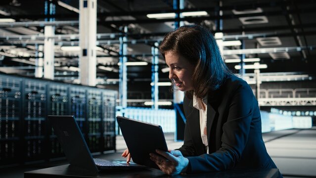 Data center software developer uses devices as control panel for digital twin simulation. Server hub female programmer using laptop and tablet to adjust blue wireframe mesh hardware settings