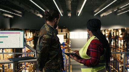 Fototapeta premium Army logistics team in uniform working in warehouse on military base, coordinating pallets distribution. Diverse officers oversee tracking systems for defense supply chain infrastructure.