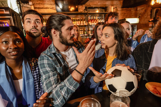Sports fans arguing and gesturing during a soccer match at a pub bar counter.
