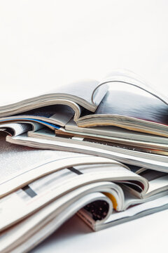 Concepto editorial: Pila de revistas abiertas sobre fondo blanco. Primer plano de varias revistas brillantes abiertas, apiladas sobre una superficie blanca y limpia, que representan los medios
