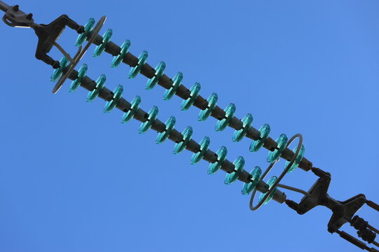 Detailed view of a high-voltage power line, captured against a clear blue sky with bright sunlight and scattered cumulus clouds. Contemporary Swedish energy infrastructure presented in sharp daylight 