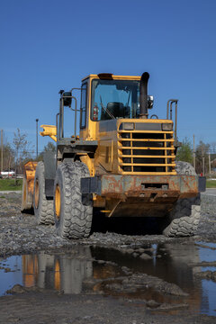 Yellow wheel loader front end on muddy construction site against blue sky