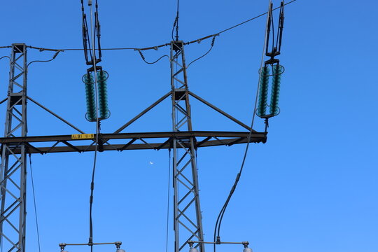 Detailed view of a high-voltage power line, captured against a clear blue sky with bright sunlight and scattered cumulus clouds. Contemporary Swedish energy infrastructure presented in sharp daylight 