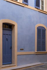 Fototapeta premium Blue door and shuttered window on pastel blue building with beige trim, exterior wall in natural light, Saint Tropez, France.