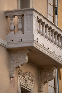 Stone balcony with balusters and decorative carvings on the exterior of a beige building. Architectural details include ornate corbels and window frame. Daylight, Saint Tropez.