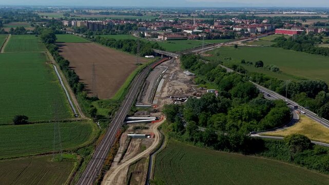 Railway construction in rural area: An aerial view captures the ongoing construction of a new railway line cutting through a verdant rural landscape, with a highway visible in the distance.