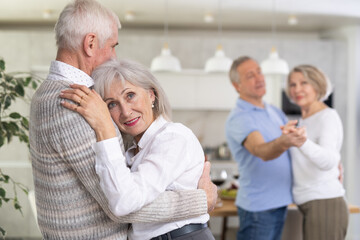 Fototapeta premium Two married couples enjoying slow dancing at a house party for friends