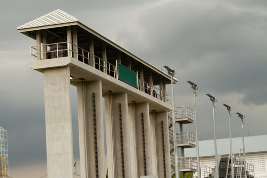 Modern floodgate control structure with dramatic cloudy sky, industrial water management architecture and elevated concrete engineering facility outdoors.