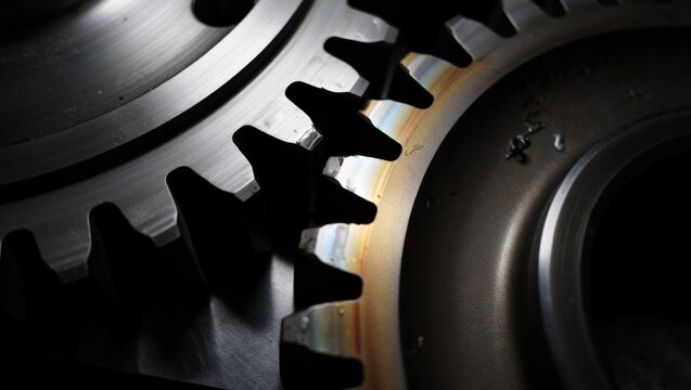 Dramatic extreme close-up of interlocking heavy industrial steel gear teeth with dark moody lighting, visible oil stains, iridescent reflections, and precise machined metal texture.
