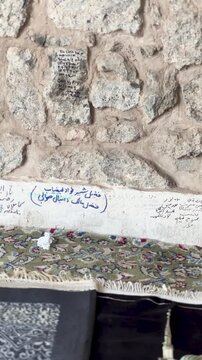 Detail shot of a historic stone wall featuring prayer rugs and handwritten names inside the Al Fath Mosque in Medina.