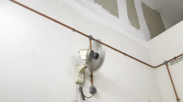 Vintage industrial wall fan oscillating and spinning in a factory workshop.