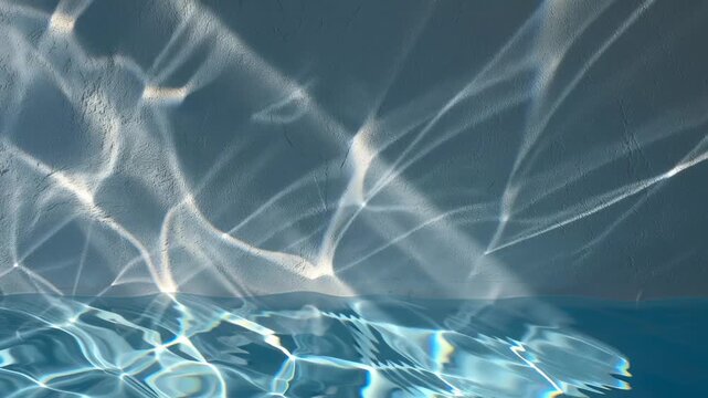 Water reflection creates an abstract light pattern on a textured wall, showcasing blue ripples and caustics. This serene liquid surface movement provides a tranquil and clean background, commercial pr