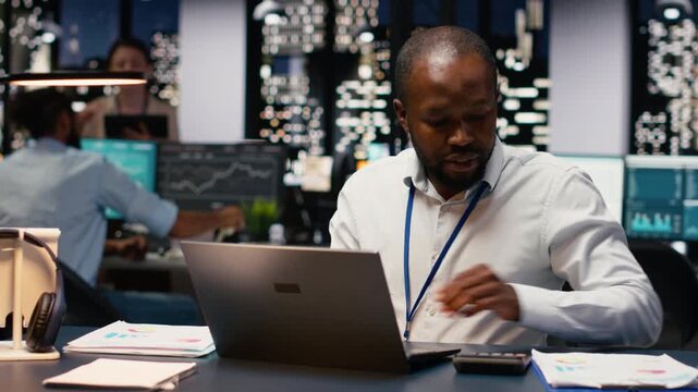 African american worker typing on laptop keyboard at office desk, doing computer tasks and working overnight. Adult man using notebook at work, finishing accounting assignment.