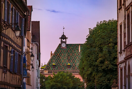 Historic Koifhus old customs building with a distinctive green and red geometric patterned tile roof with a clock tower in Colmar, France at sunset