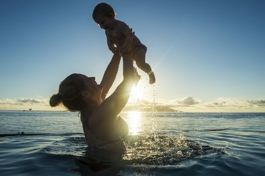 Mother playing with her little baby in the water at sunset, Papeete, Tahiti