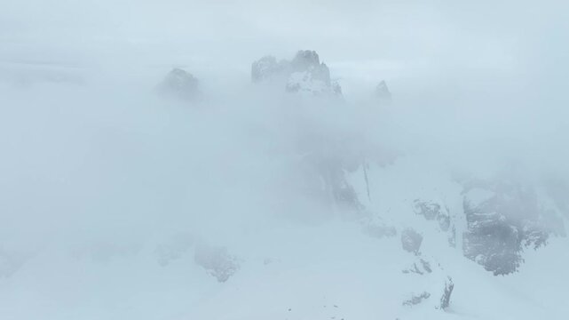 Aerial view of snow-covered peaks of Parco Naturale Paneveggio Pale di San Martino shrouded in thick clouds in Primiero San Martino di Castrozza, Trentino-Alto Adige, Italy.