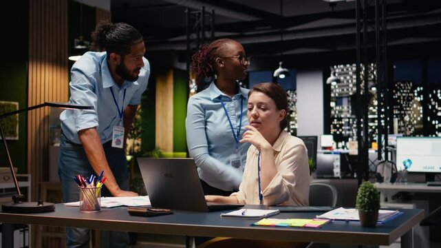 Corporate team gathered around office desk collaborating on project and sharing business intelligence insights. Group working late into the night, focusing on forecasting and task management.