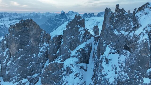Aerial view of the snow-covered Parco Naturale Paneveggio Pale di San Martino peaks under a soft twilight sky in Primiero San Martino di Castrozza, Trentino-Alto Adige, Italy.