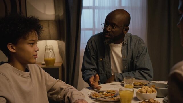 Handheld shot of family conflict scene strict father scolding teenage boy for using smartphone at dinner table, gadget addiction in children, copy space