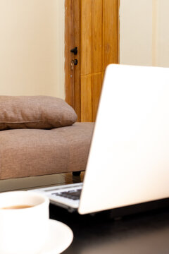 ow angle view of a remote workspace setup with a laptop, coffee mug, and a sofa couch in the background