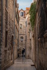 Fototapeta premium Epic traditional old town narrow street ancient architecture vertical panorama. Cinematic low angle view of historic medieval limestone house facades, cobblestone pavement road, stone archway and co