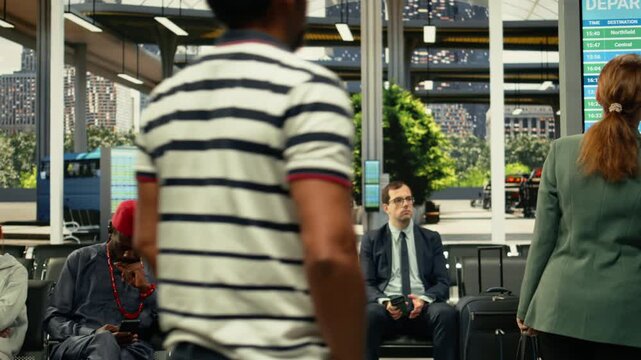Diverse passengers in crowded bus station for long-distance interstate journey, checking departure board timetable. Travelers with luggage and carry-on bags waiting for international coach.