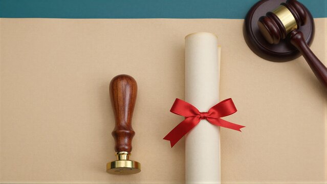 Wooden gavel scroll with red ribbon and seal on beige paper.