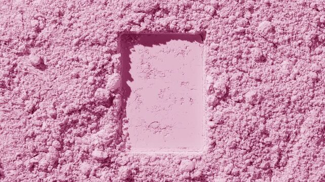 Top-down capture of light pink natural powder surface with a rectangular shape pressed in by rotating light source producing shifting shadows