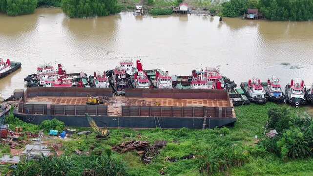 Aerial view of tugboats parked in a row on the riverbank next to barges