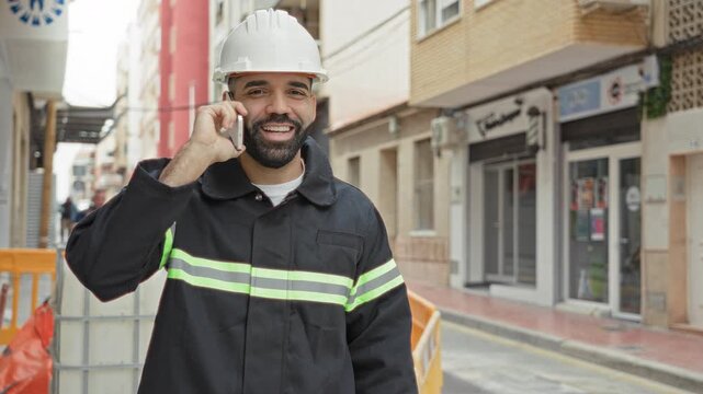 Man engineer holding smartphone talking on a street worksite wearing hardhat and reflective vest; confidence.