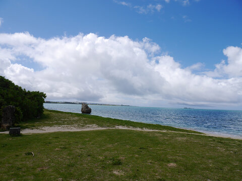 Green lawn with lone sea rock and turquoise ocean 
under dramatic clouds, Senaga Island, Tomigusuku, Okinawa, Japan