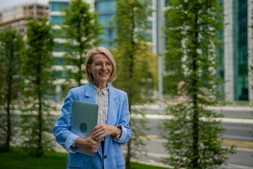 Mature businesswoman holding laptop walking in city park © Jelena