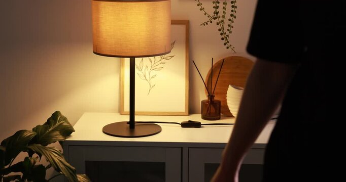 Woman turning on lamp with inline cord switch at cabinet near white wall indoors, closeup