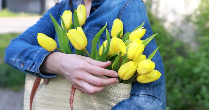 Woman in shirt holding wicker bag with beautiful tulip flowers outdoors, closeup. Camera moving forward
