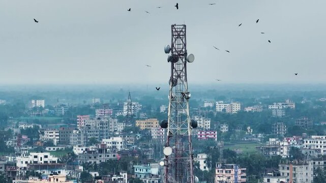 Aerial view of a telecommunications tower with a technician climbing among satellite dishes and birds flying over a dense urban landscape.