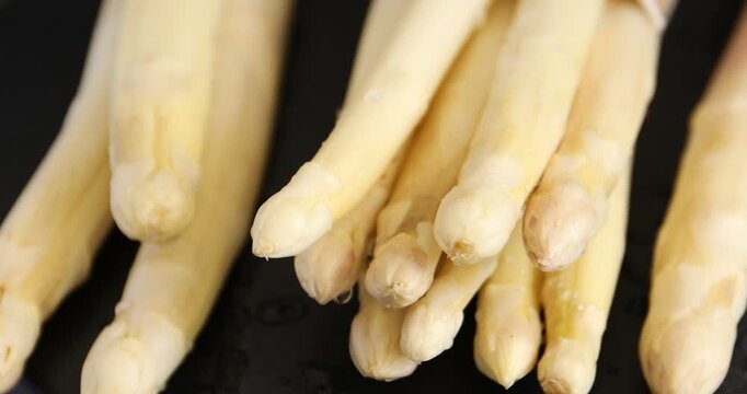 Dripping water onto raw white asparagus spears on black table, closeup