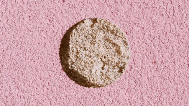 Top-down capture of beige powder natural texture exposed through a round opening in the surface covered with pink sifted powder, lit by moving light casting shadows | Blush promotional concept