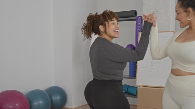 Woman shaking hands with friend by whiteboard and yoga props, foam rollers and exercise balls in fitness studio; friendship support joy.