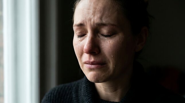 A close-up portrait of a woman crying with tears streaming down her face, conveying deep sadness and emotional distress.