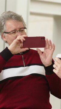 Vertical video: Bringing phone up, man in maroon sweater composing shot on porch, holding red phone