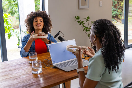 African American women in denim sharing over-ear headset while testing audio on laptop at home desk
