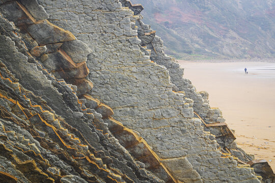 View of the unique flysch rock formations and a person walking on the sandy beach at Playa de Sopelana in Vizcaya, Pais Vasco, Spain.