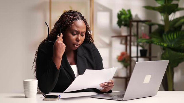 African corporate businesswoman concentrating on documents and laptop in a modern office