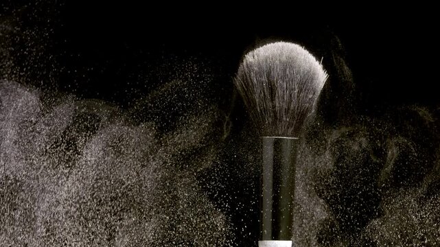 Extreme close-up slow motion shot of a black brush flicking light beige powder against a simple black backdrop | Concept for a powder foundation advertisement campaign idea